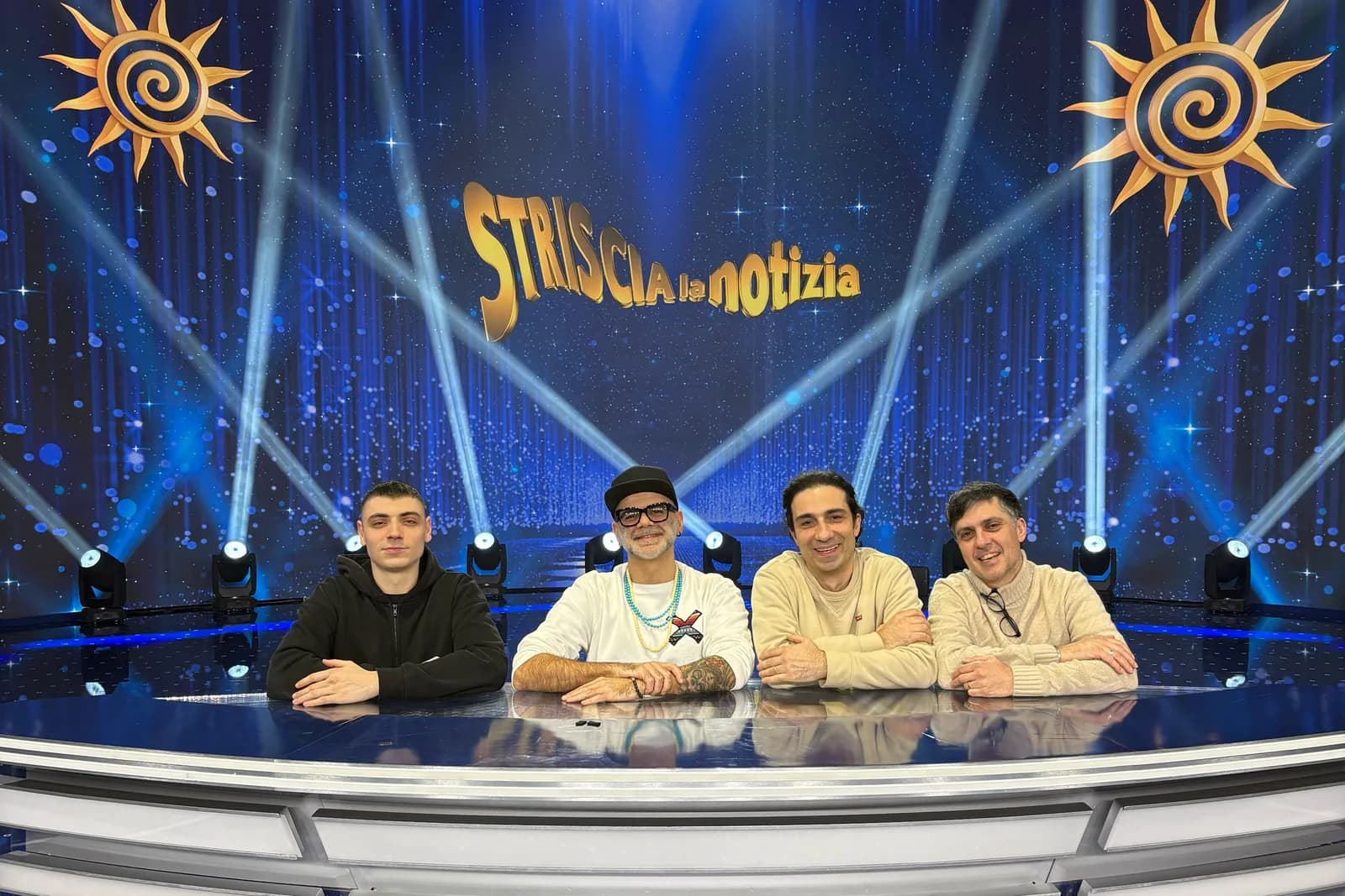 Alessandro Bigatti e tre persone del team seduti al bancone dello studio, davanti al LED con il logo di Striscia la Notizia
